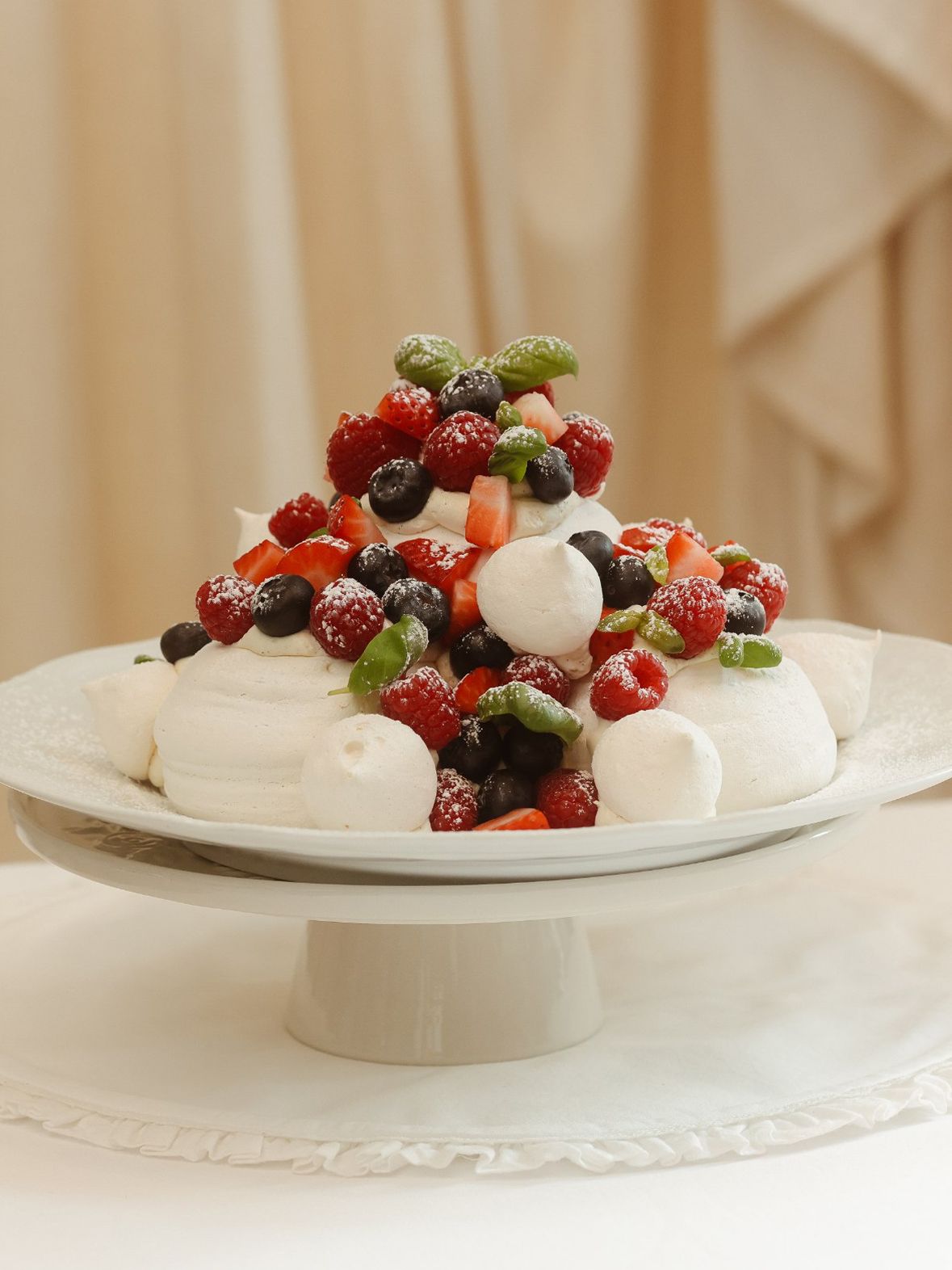 A pavlova crowned with fresh berries on a white cake stand at Bisou.