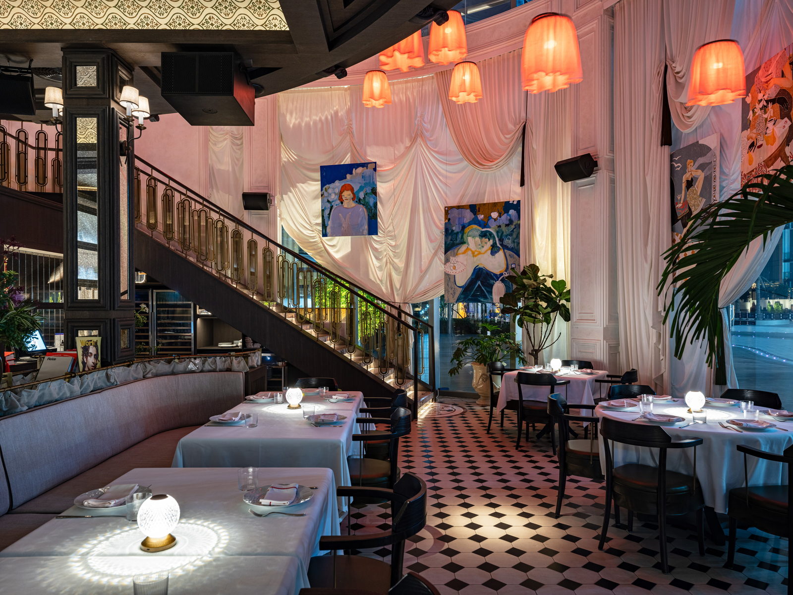 A dinner table at Bisou dressed in white linen under the pleated coral lamps, with the brass staircase and the Opera District windows behind.