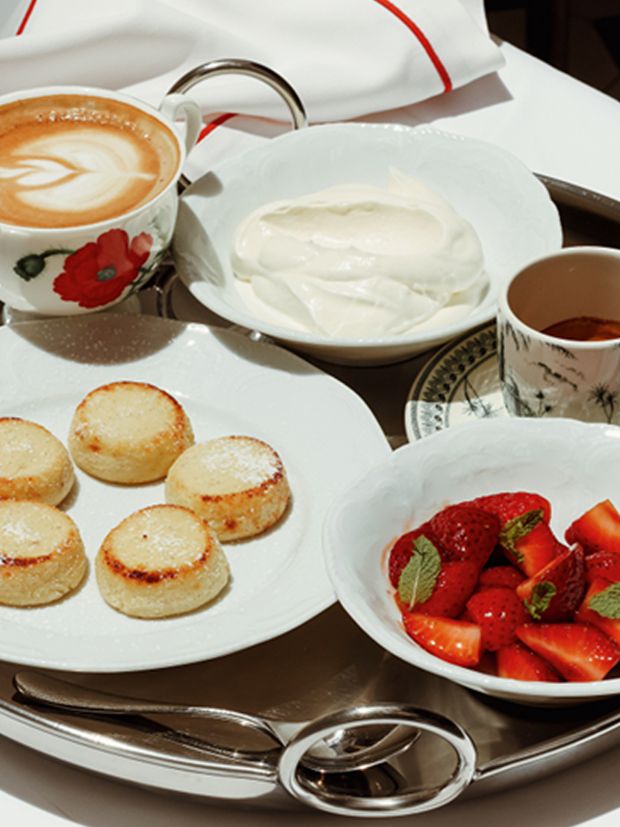 A Bisou breakfast laid out — coffee, syrniki, cream and strawberries on white linen.