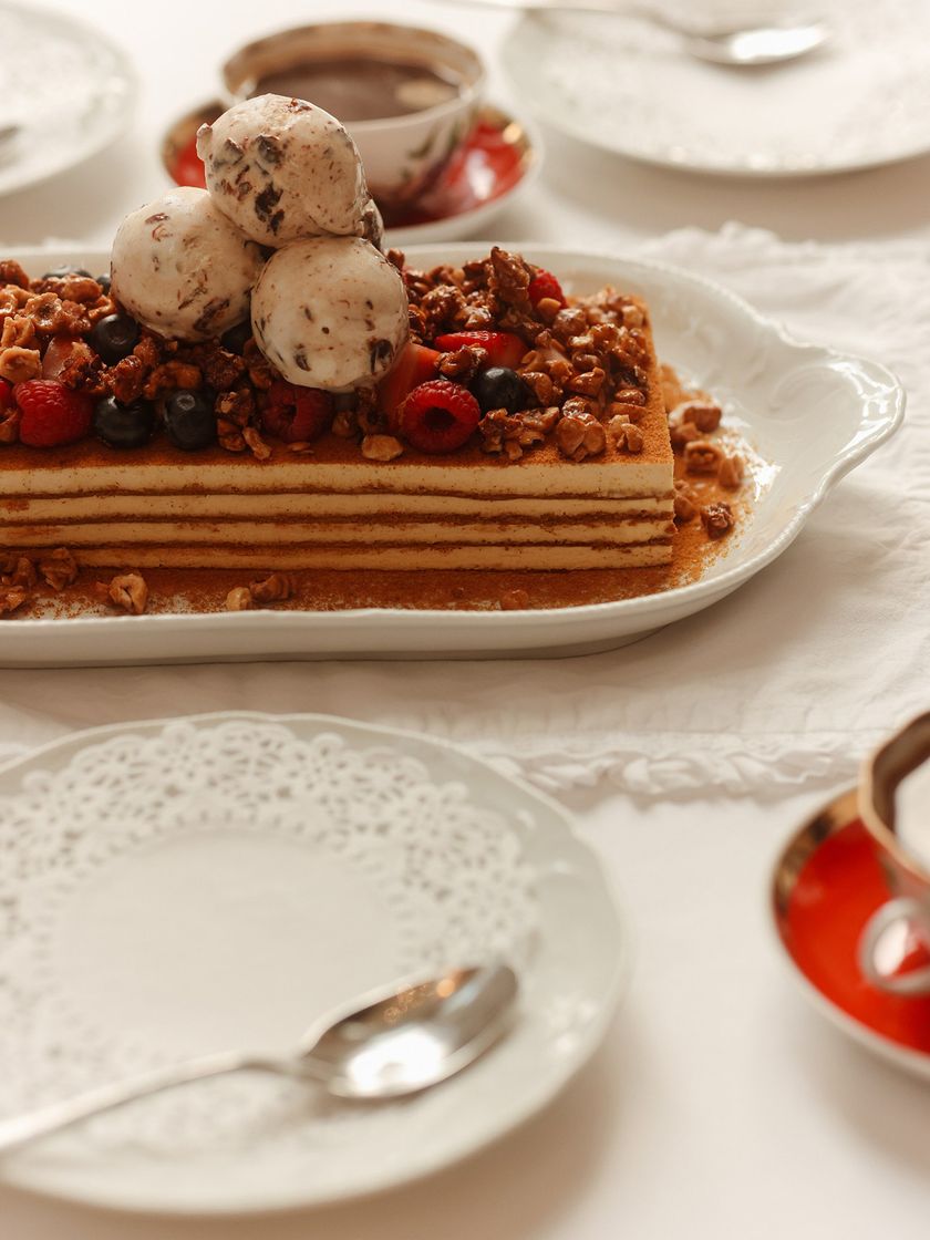 A layered Bisou honey cake with berries and ice cream on a white plate.