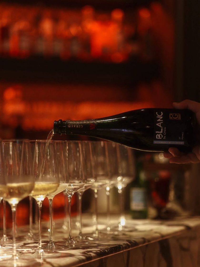 Champagne poured into a row of coupes at the Bisou bar, the red-lit shelves behind.